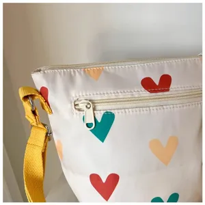 Detail shot of cute canvas crossbody bag featuring colorful heart print and yellow strap.