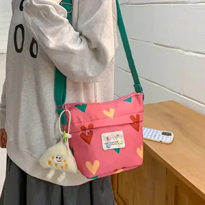 Cute pink canvas crossbody bag with heart pattern and green strap for daily student use.