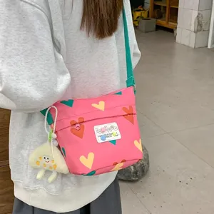 Pink canvas crossbody bag for women, cute heart pattern daily shoulder bag with plush pendant.