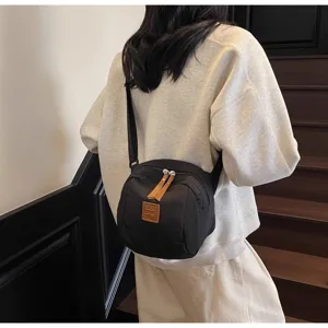 Vue détaillée d'un sac bandoulière en nylon décontracté avec fermeture éclair et patch en cuir.