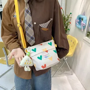 Cute canvas crossbody bag for women with colorful heart print, yellow strap and plush pendant.