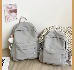 Grey casual minimalist backpack detail showing front pocket and cute plush pendant charm.