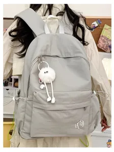 Detail shot of casual solid color backpack with cute plush pendant and multiple functional pockets.