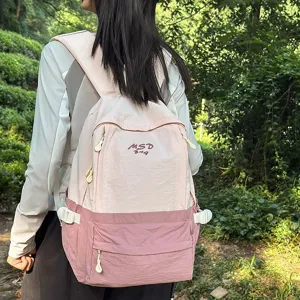 Outdoor detail of a lightweight pink two-tone backpack worn by a model, showing straps.