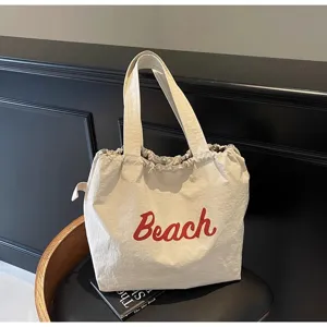 Vista detallada del bolso tote de lona beige con texto rojo Beach para viajes y trabajo diario.