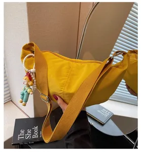 Lässige gelbe Nylon Damentasche Umhängetasche mit Puppenanhänger und breitem Gurt.