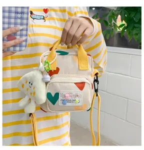 Close-up detail of cute canvas crossbody bag with colorful hearts, yellow handles and plush pendant.