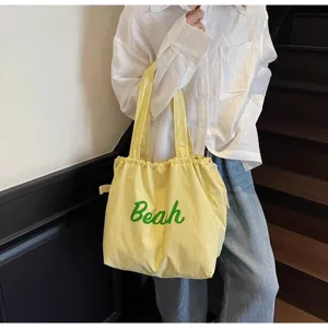 Vista detallada del bolso tote de lona amarilla con estampado verde, llevado al hombro.