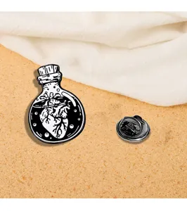 Detail shot of gothic punk heart in bottle metal brooch pin, black white enamel lapel.