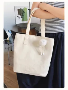 Detail view of cream canvas tote bag with cute plush pendant for daily casual commuting.