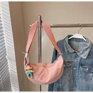 Detailansicht der lässigen rosa Umhängetasche mit süßem Cartoon-Puppenanhänger am Ständer.