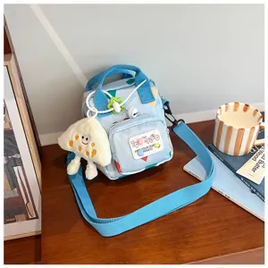 Detailed view of light blue canvas crossbody mini bag with cartoon print and front pocket charm.