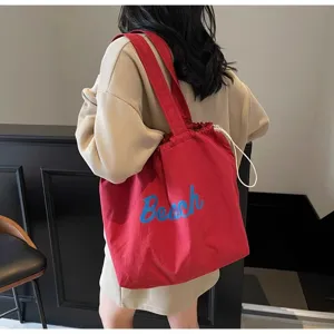 Vista detallada del bolso tote de lona roja con estampado Beach y cierre de cordón