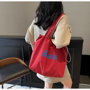 Vista detallada de un bolso tote de lona roja con texto azul, llevado en interiores.