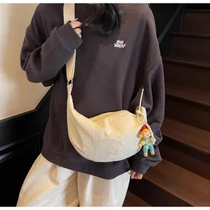 Detailaufnahme der lässigen Canvas Umhängetasche in Beigeweiß mit süßem Puppenanhänger.