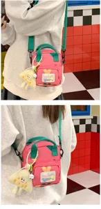 Detailed shot of cute pink and green canvas crossbody bag with plush charm and front pocket.