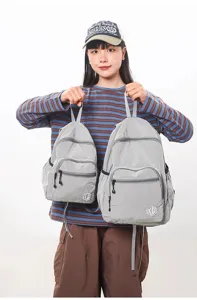 Detail view of lightweight waterproof grid backpacks in two sizes, held by model in studio.