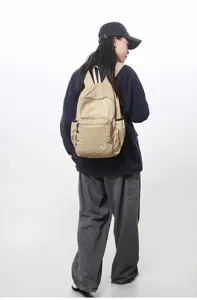 Detail view of a lightweight minimalist casual backpack in khaki, worn by a model.