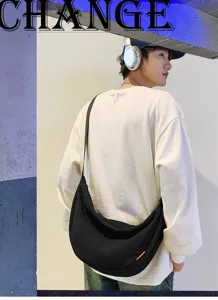 Detailed view of the casual black crossbody dumpling bag worn by a stylish young male model.