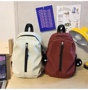 Detailed view of casual lightweight backpacks in beige and wine red with cute furry pendants.
