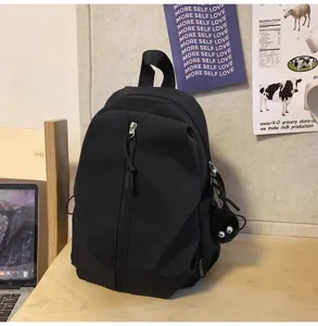 Detail shot of lightweight black casual backpack with front zipper pocket and charm.