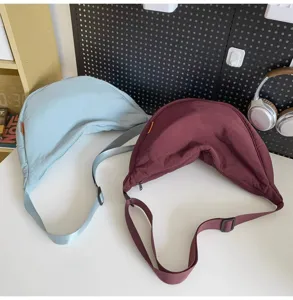 Detail shot of two casual crescent crossbody bags in light blue and dark red on white desk.