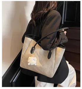 Detailansicht einer schicken Beigefarbenen Tasche mit schwarzen Griffen und Plüschanhänger.