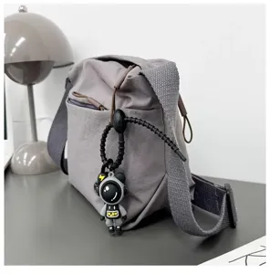 Grey nylon crossbody bag with wide strap, front pocket and astronaut pendant detail.