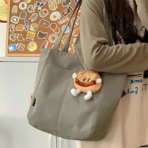Detail shot of casual grey canvas tote bag featuring cute plush burger pendant and pocket.