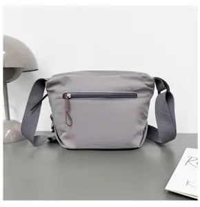 Detail view of grey nylon crossbody bag, showcasing zipper pocket and adjustable strap.