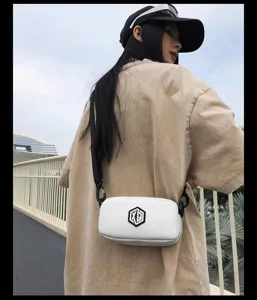 Detailed outdoor shot of a compact white crossbody phone bag worn by a fashion model.