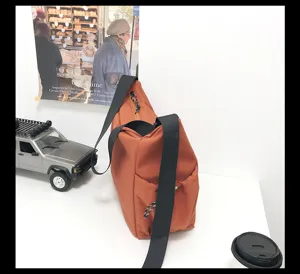 Close-up of casual canvas crossbody bag in rust brown, showing side pocket and sturdy black strap.