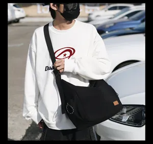 Casual black canvas messenger bag detail view, showing durable wide strap and side zip pocket design.