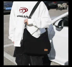 Detail view of casual black canvas messenger bag, showing durable fabric and wide strap.