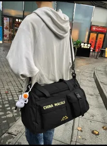 Straßendetail der schwarzen Reisetasche mit Vordertasche, robustem Material und Enten-Anhänger.
