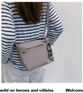 Grey nylon crossbody bag detail showing zipper pocket and cute astronaut keychain.