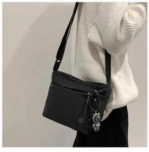 Detail view of lightweight nylon crossbody bag in black, casual messenger style with charm.