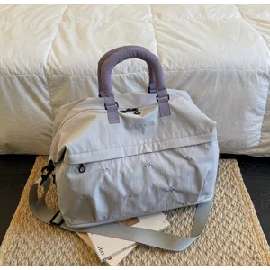 Detailed view of a lightweight grey travel duffel bag featuring purple handles and cute bow embroidery.