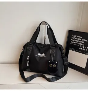 Detailansicht der schwarzen Reisetasche mit niedlichem Plüschkatzen-Anhänger und Gurt.