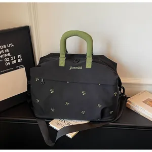 Detailed close-up view of the black travel bag with green handles and embroidery details.