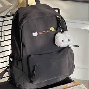 Close-up of black cute school backpack with cat embroidery and fluffy plush pendant detail.