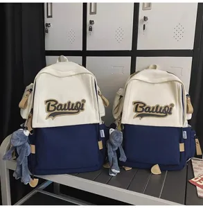 Close-up detail of the contrast color school backpack featuring logo embroidery and cute doll charm.