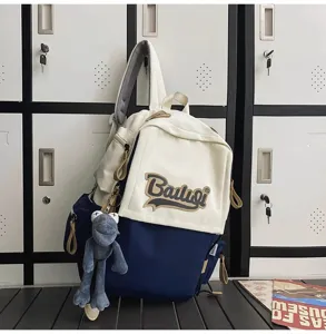 Two-tone canvas backpack with front pocket and cute plush toy pendant for daily school and travel use.