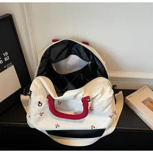 Detailed view of large white travel duffel bag with red handles and cute bow embroidery.