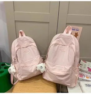 Detailed view of casual pink dual-shoulder backpack with cute plush pendant and front pocket.