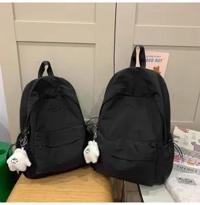 Detail view of casual black backpack with cute plush pendant, simple daily school bag for students.