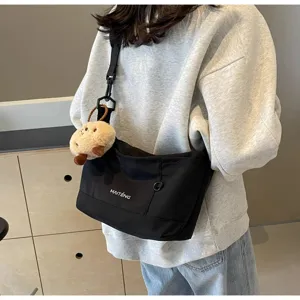 Detail view of black canvas messenger bag with adjustable strap and cute plush doll charm.