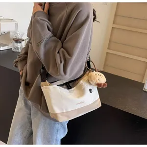 Retro canvas crossbody bag for women, casual two-tone messenger bag with cute plush pendant.