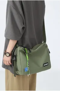 Military green canvas messenger bag detail showcasing durable fabric, strap, and decorative tags.