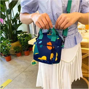 Canvas crossbody bag detail showing colorful abstract print, green straps and cute frog charm.